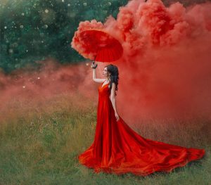 Beautiful woman in red dress holding an umbrella and red-colored smoke bomb