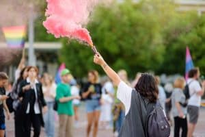 Person holding a colored smoke bomb during pride parade.