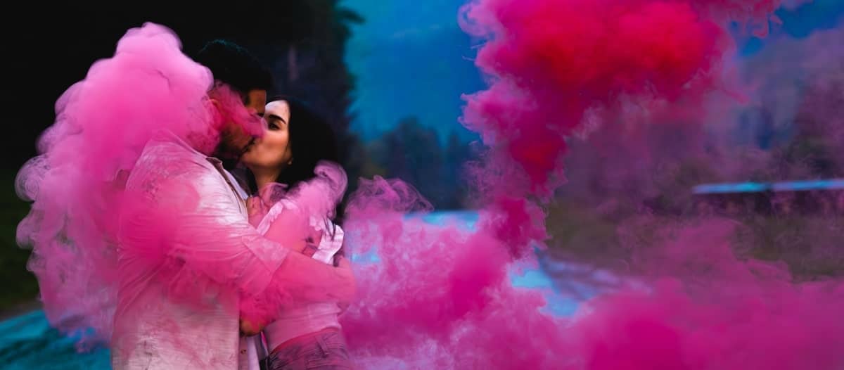 Young couple kissing while holding a pink-colored smoke bomb